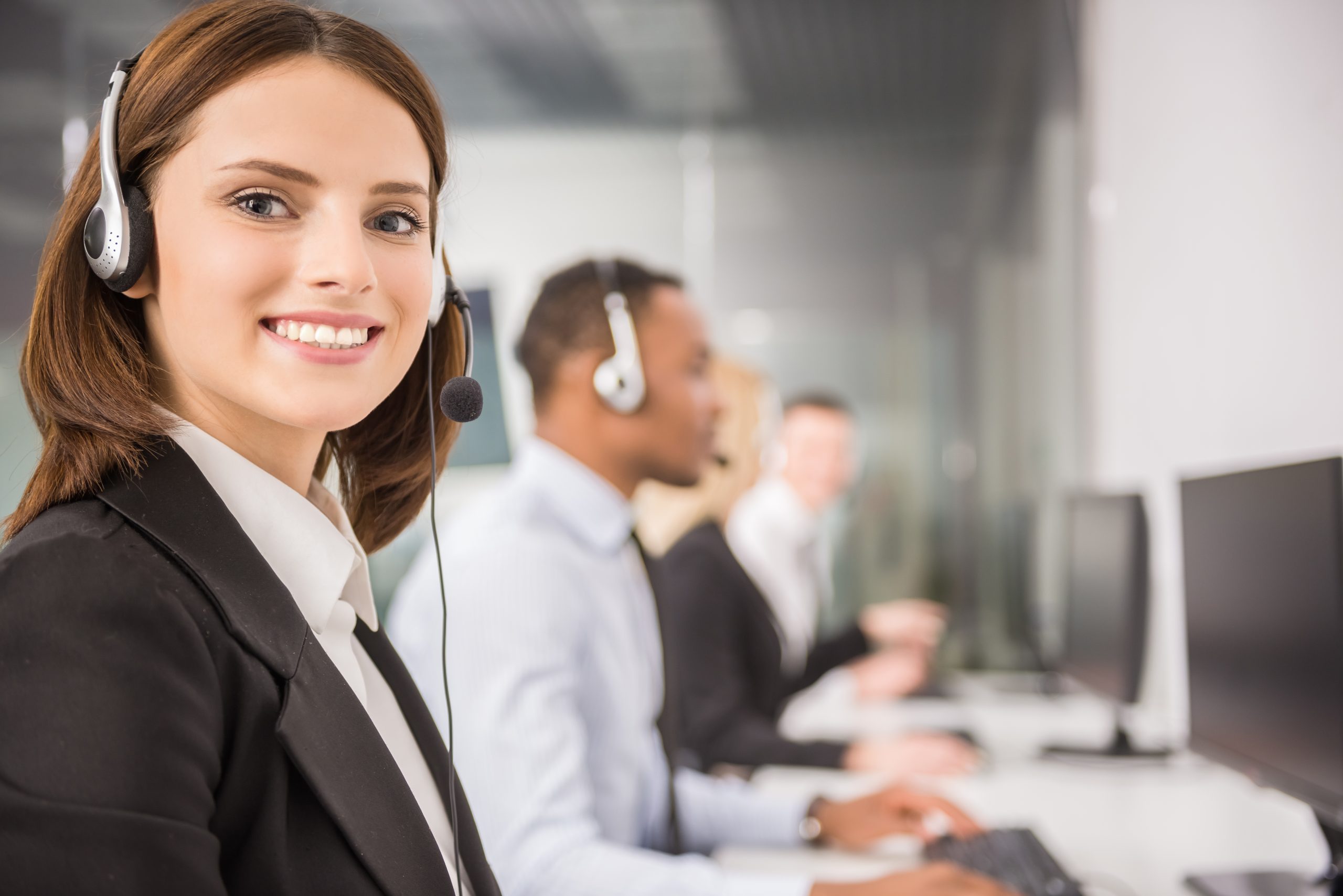 Attractive young woman in suit sitting at call center office with colleagues and working.